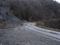 a wet road with gravel on the side and a train coming down the hill below