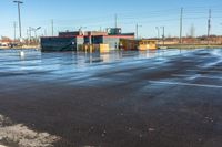 wet sidewalk next to parking lot with gas station and building in background and empty road