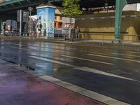 a wet street with the road light on, and an overpass above it and traffic signs along side