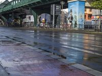 a wet street with the road light on, and an overpass above it and traffic signs along side