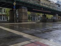 a bridge with an elevated walkway over a wet street in the city at day time