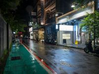 a wet street at night with a motorcycle parked on the sidewalk beside it and a building near by