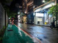 a wet street at night with a motorcycle parked on the sidewalk beside it and a building near by