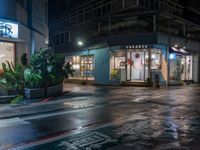 a wet street is outside of an office building at night with rain running down the road