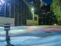 fire hydrant on a wet surface next to an illuminated stadium building with trees in the background