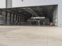 a white commercial aircraft is parked outside a hangar and a white car is parked inside a hangar