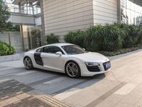 a white audi sports car parked on a city sidewalk with greenery in the background