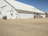 a photo of a white barn that is outside of it's yard, and there is an open space with barrels