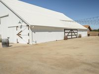 a photo of a white barn that is outside of it's yard, and there is an open space with barrels