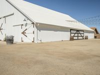 a photo of a white barn that is outside of it's yard, and there is an open space with barrels