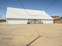 a white barn and a large open space at the bottom of it has strings hanging from the roof