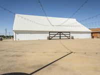 a white barn and a large open space at the bottom of it has strings hanging from the roof