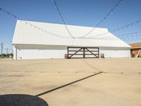 a white barn and a large open space at the bottom of it has strings hanging from the roof