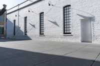 two windows that are on a white brick building with a gray sidewalk and a red fire hydrant