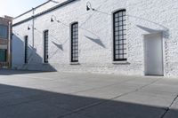 two windows that are on a white brick building with a gray sidewalk and a red fire hydrant