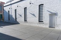 two windows that are on a white brick building with a gray sidewalk and a red fire hydrant