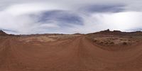 a 360 - angle picture taken on the dirt road shows the rolling terrain in front of the sky and the clouds above