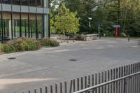 a white dog is walking down the concrete pathway towards a building with glass windows and trees