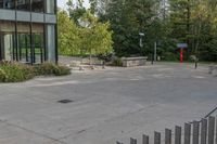 a white dog is walking down the concrete pathway towards a building with glass windows and trees