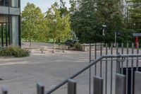 a white dog is walking down the concrete pathway towards a building with glass windows and trees