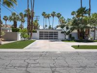 a white garage with three garages sitting next to palm trees and grass covered streets