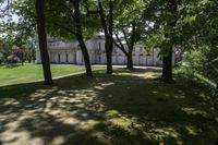 large white house with several trees in a grassy area near it and another building in the distance