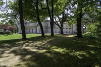 large white house with several trees in a grassy area near it and another building in the distance