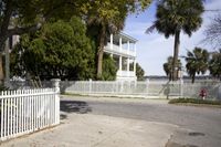 a white house in the middle of the street with lots of trees in front of it