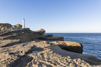 a white lighthouse sitting on top of a rocky cliff next to the ocean with the sun shining