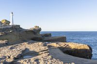 a white lighthouse sitting on top of a rocky cliff next to the ocean with the sun shining