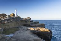 a white lighthouse sitting on top of a rocky cliff next to the ocean with the sun shining