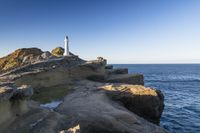 a white lighthouse sitting on top of a rocky cliff next to the ocean with the sun shining