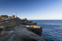 a white lighthouse sitting on top of a rocky cliff next to the ocean with the sun shining