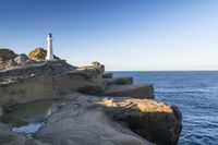 a white lighthouse sitting on top of a rocky cliff next to the ocean with the sun shining