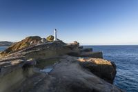 a white lighthouse sitting on top of a rocky cliff next to the ocean with the sun shining