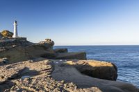 a white lighthouse sitting on top of a rocky cliff next to the ocean with the sun shining