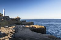 a white lighthouse sitting on top of a rocky cliff next to the ocean with the sun shining