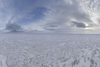 the ground covered in white snow under cloudy skies by an open field with tracks of ice