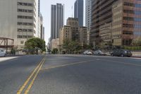 city street in a wide urban area surrounded by tall buildings and trees with traffic passing on the road