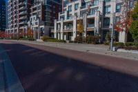 a wide empty city street in front of modern apartment buildings, and empty sidewalk with street lights