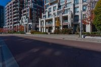 a wide empty city street in front of modern apartment buildings, and empty sidewalk with street lights