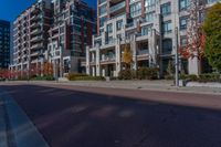 a wide empty city street in front of modern apartment buildings, and empty sidewalk with street lights