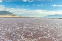 this photo is of a wide desert plain covered in salt and sky with large mountains behind it