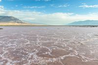 this photo is of a wide desert plain covered in salt and sky with large mountains behind it