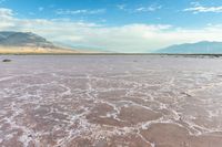 this photo is of a wide desert plain covered in salt and sky with large mountains behind it