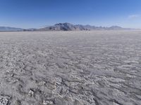 a wide expanse of land with low mountain and sky background, showing blue sky, mountains, and a few large patches of white cloudy dirt