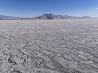 a wide expanse of land with low mountain and sky background, showing blue sky, mountains, and a few large patches of white cloudy dirt