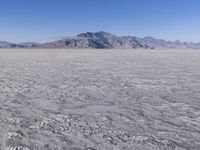 a wide expanse of land with low mountain and sky background, showing blue sky, mountains, and a few large patches of white cloudy dirt