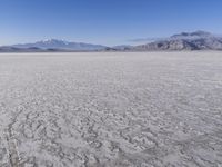 a wide expanse of land with low mountain and sky background, showing blue sky, mountains, and a few large patches of white cloudy dirt