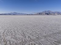 a wide expanse of land with low mountain and sky background, showing blue sky, mountains, and a few large patches of white cloudy dirt